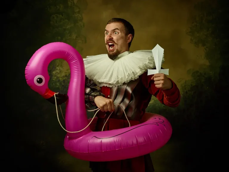 Man wearing old fashioned clothing holding a paper sword and inside a pink flamingo shape pool ring.