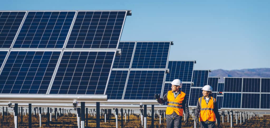 Man and woman in protective gear walking through a field of solar panels. 